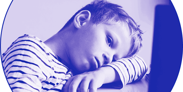 Distracted young boy, head resting on arm, aimlessly looking at a computer screen